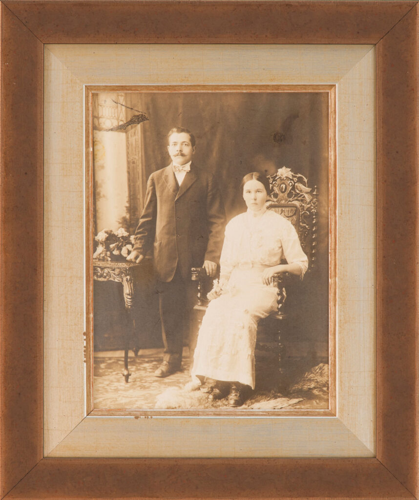 Antique sepia portrait of a man standing beside a seated woman in a layered mat and brown custom wooden frame.